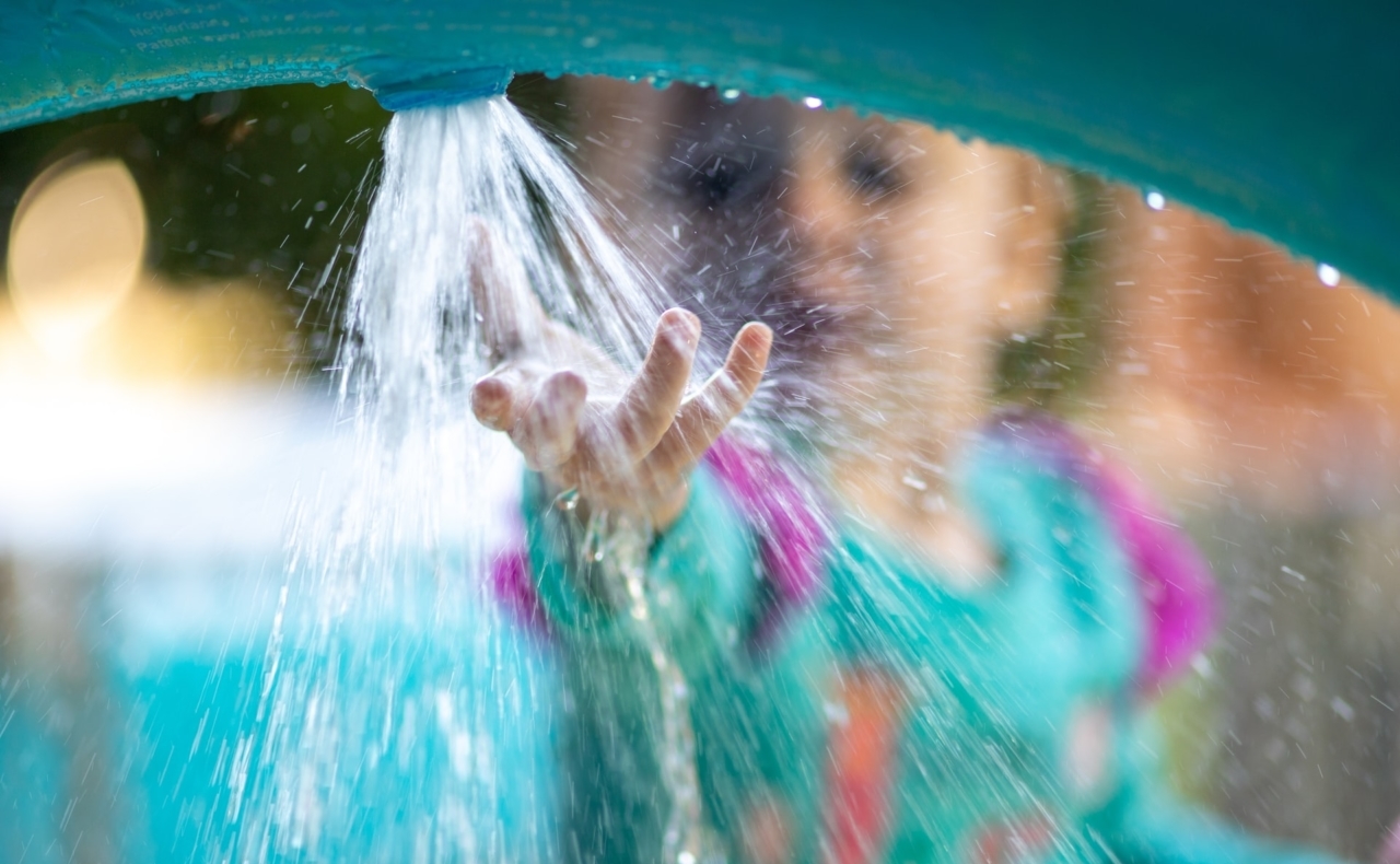 een kind houdt de hand onder een waterstraal