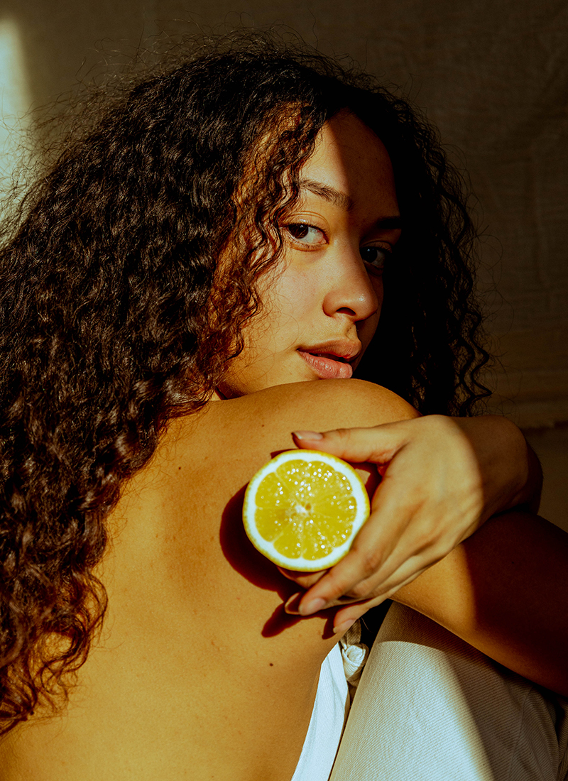 model Melissa Lewis kijkt achterom en houdt met haar hand een schijf citroen vast