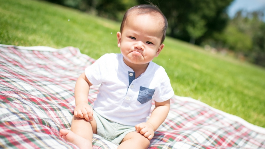 een baby zit boos kijkend op een plaid in het gras