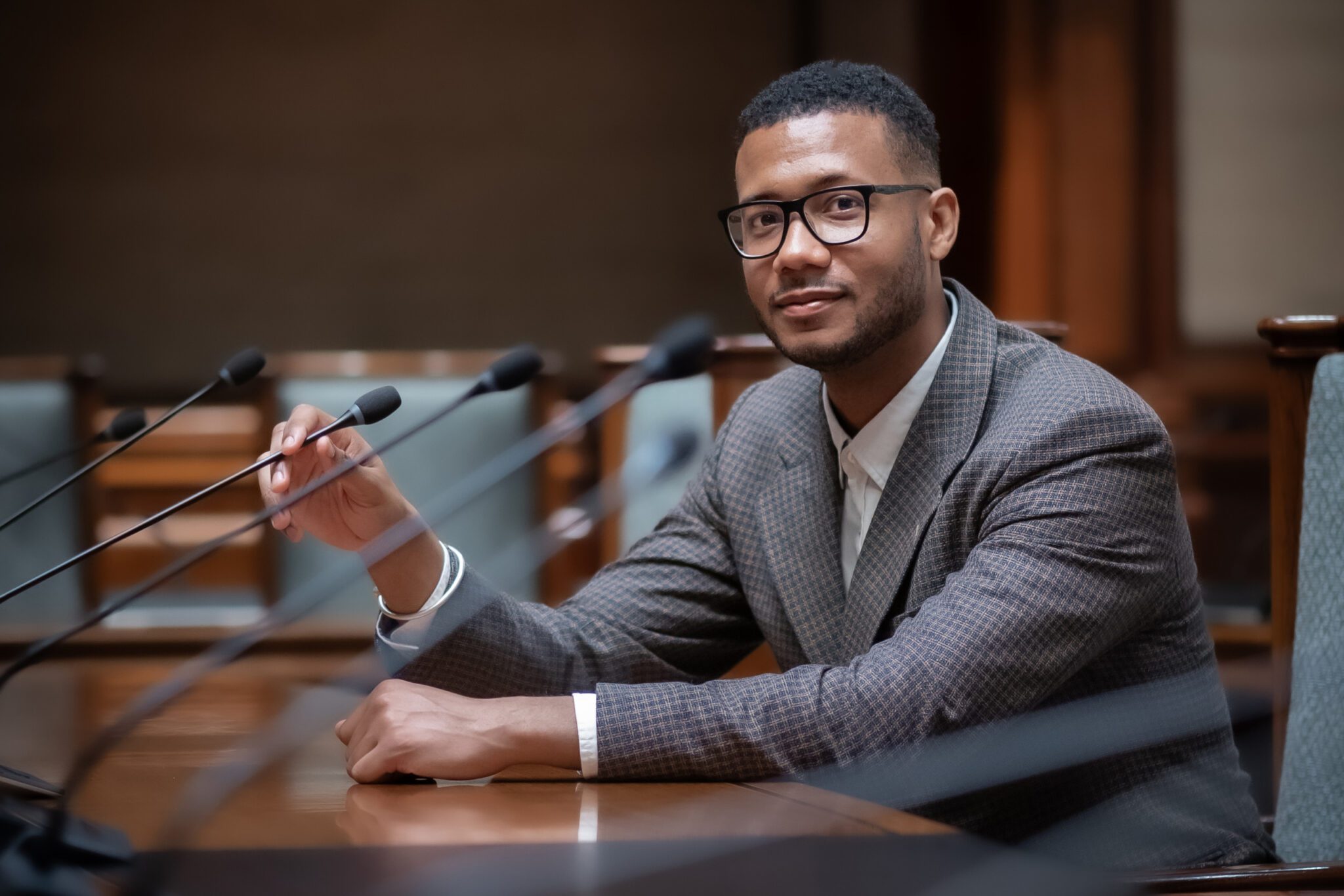 Malcolm Jones zit achter een tafel met microfoons