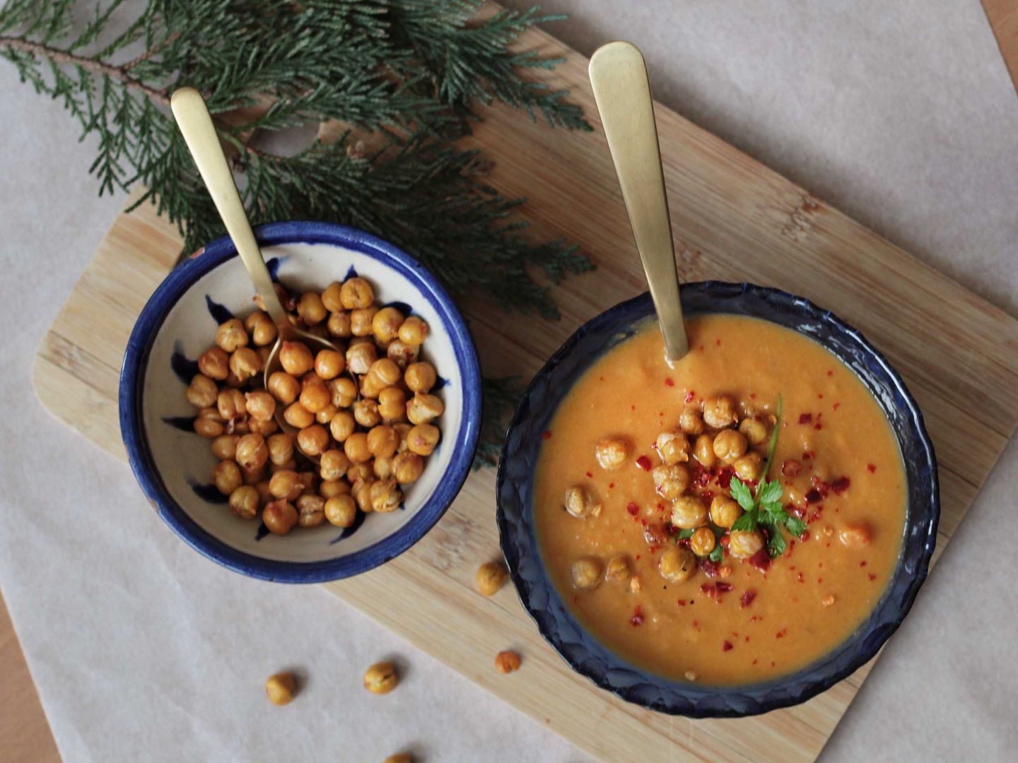 Romige-zoete-aardappelsoep-met-geroosterde-kikkererwten Een kom romige zoete aardappelsoep met daarnaast een kom met geroosterde kikkererwten