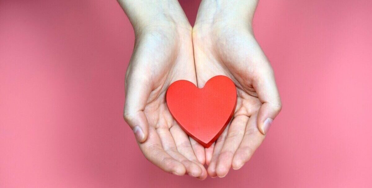 Twee handen tegen elkaar met daarin een rood hart.