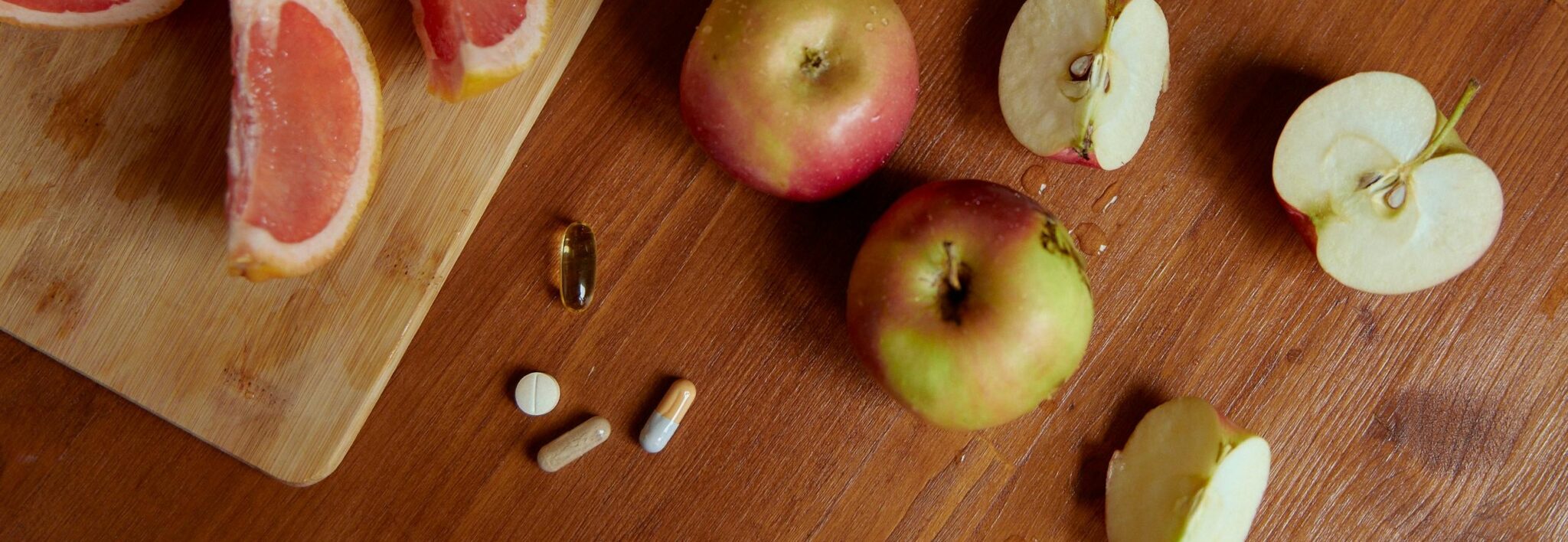 een paar doorgesneden appels, grapefruits en vitaminepillen op een tafel