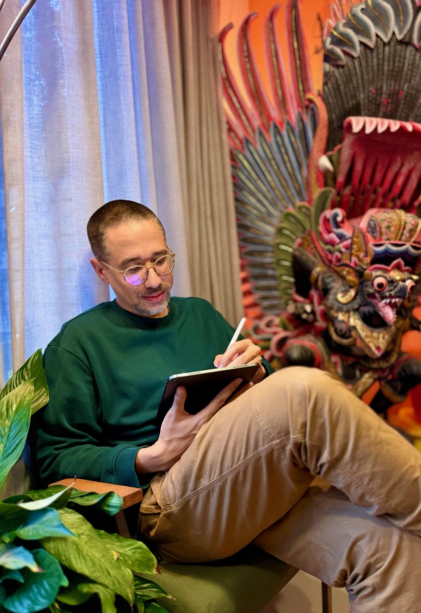 portret-melroy-bisel-van-lekkermenselijk Melroy Bisel van @lekkermenselijk, schrijvend, met rechts van hem planten en links van hem een afbeelding van Indische maskers
