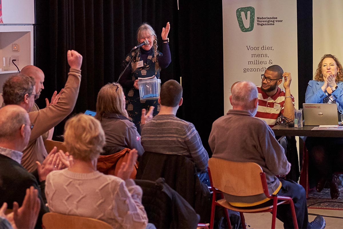 Vergadering met spreker en juichende mensen.