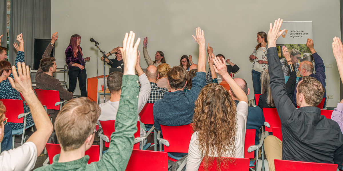 Foto van mensen die hun hand opsteken om te stemmen tijdens de ledenvergadering van de NVV op 23 maart 2025.