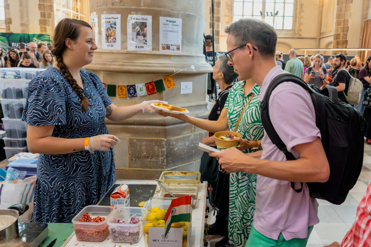 Hey-Groentje-NLVeganFair2024 Iemand geeft een bordje met eten erop aan iemand anders.